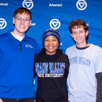 Three GVSU alum standing in front of blue backdrop, smiling at camera